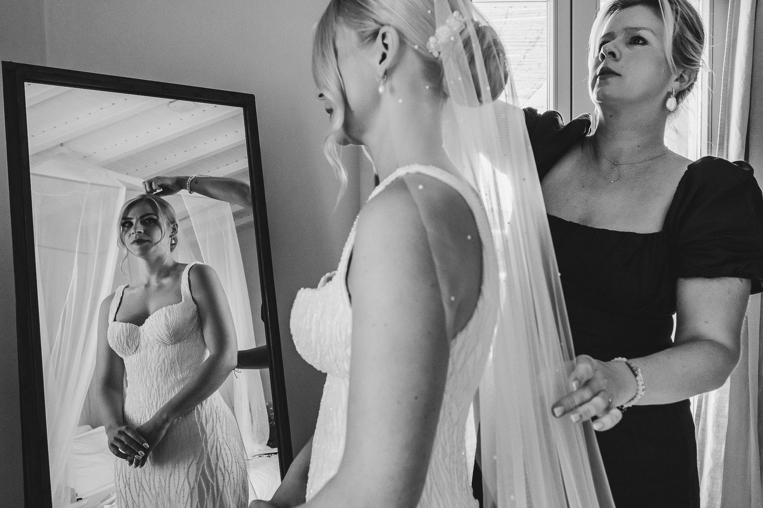 Bride and bridesmaids in white and black dresses laugh together while getting ready on wedding day.