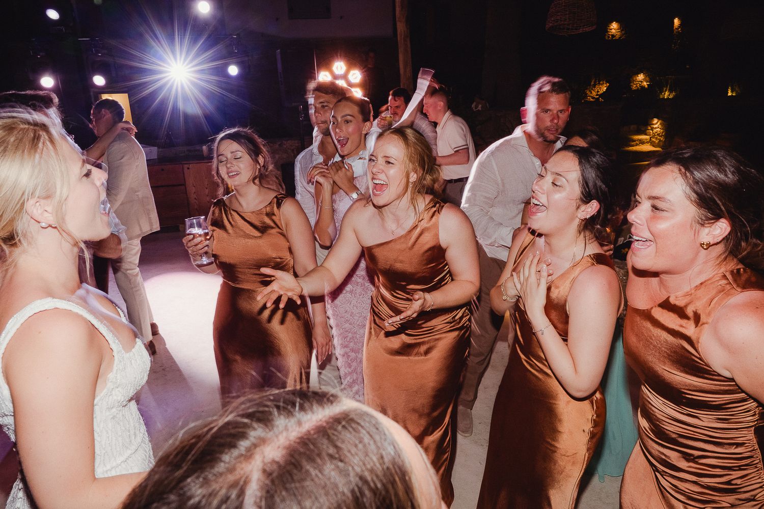 People dancing together at a wedding reception under glowing lights and decorations on a packed dance floor.
