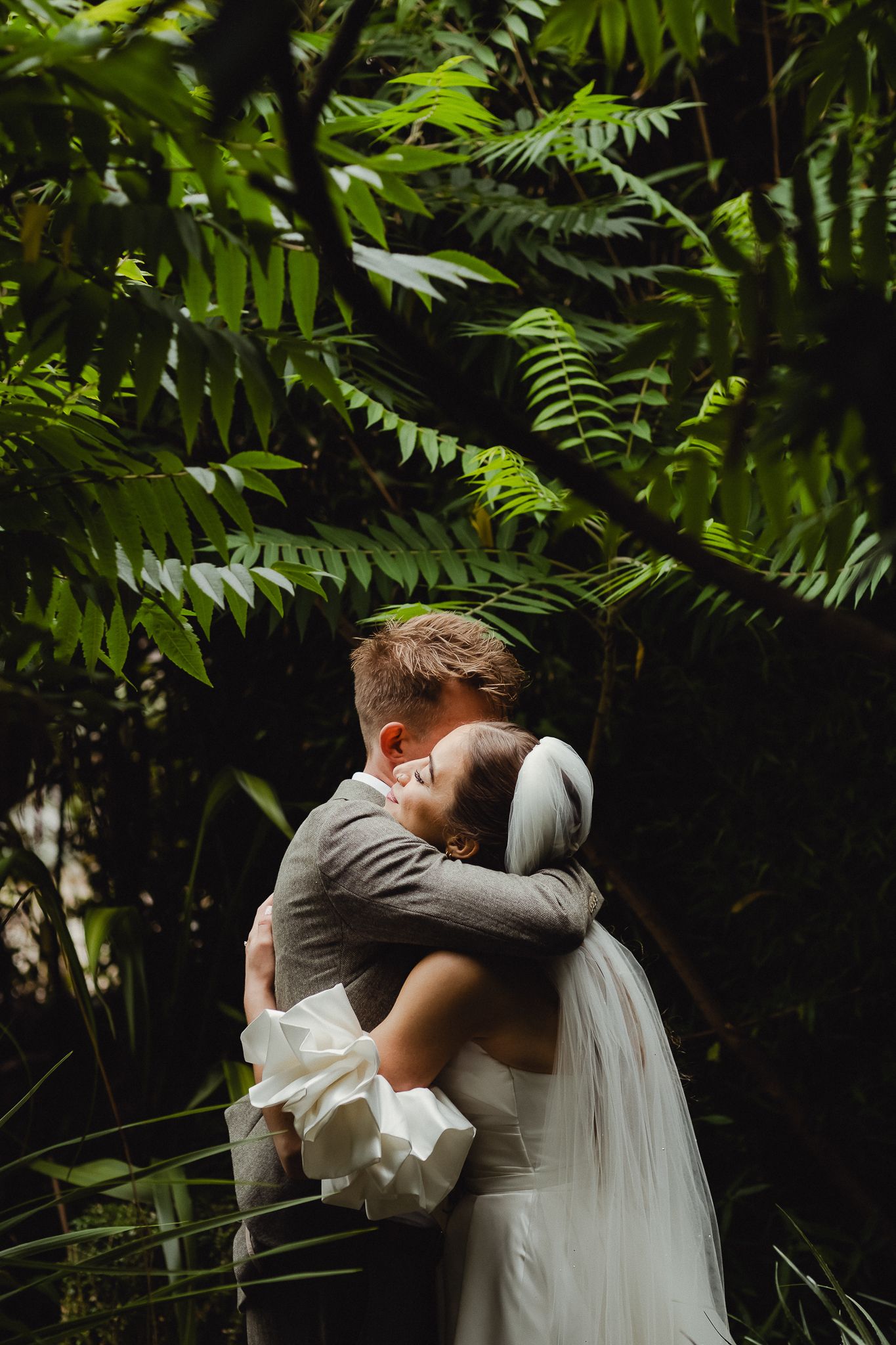 A couple embraces in a lush tropical garden setting during a wedding ceremony.