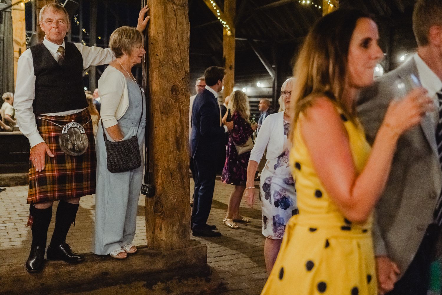 People dancing and celebrating at a rustic barn wedding reception with wooden beams and festive lighting.