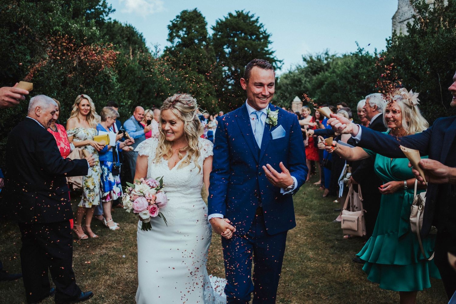 Wedding party walks through shower of confetti on outdoor garden path.