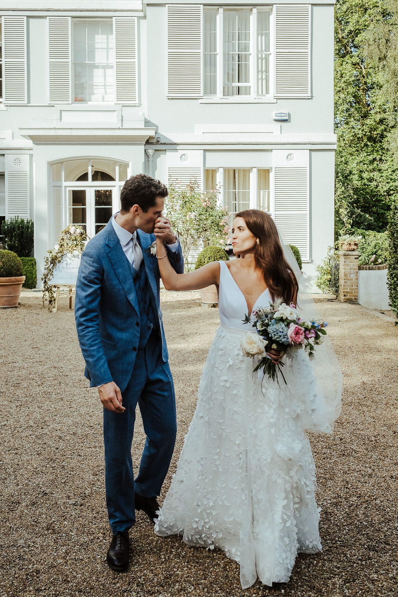 Joyful couple shares a playful moment outside a classic white home on their wedding day.