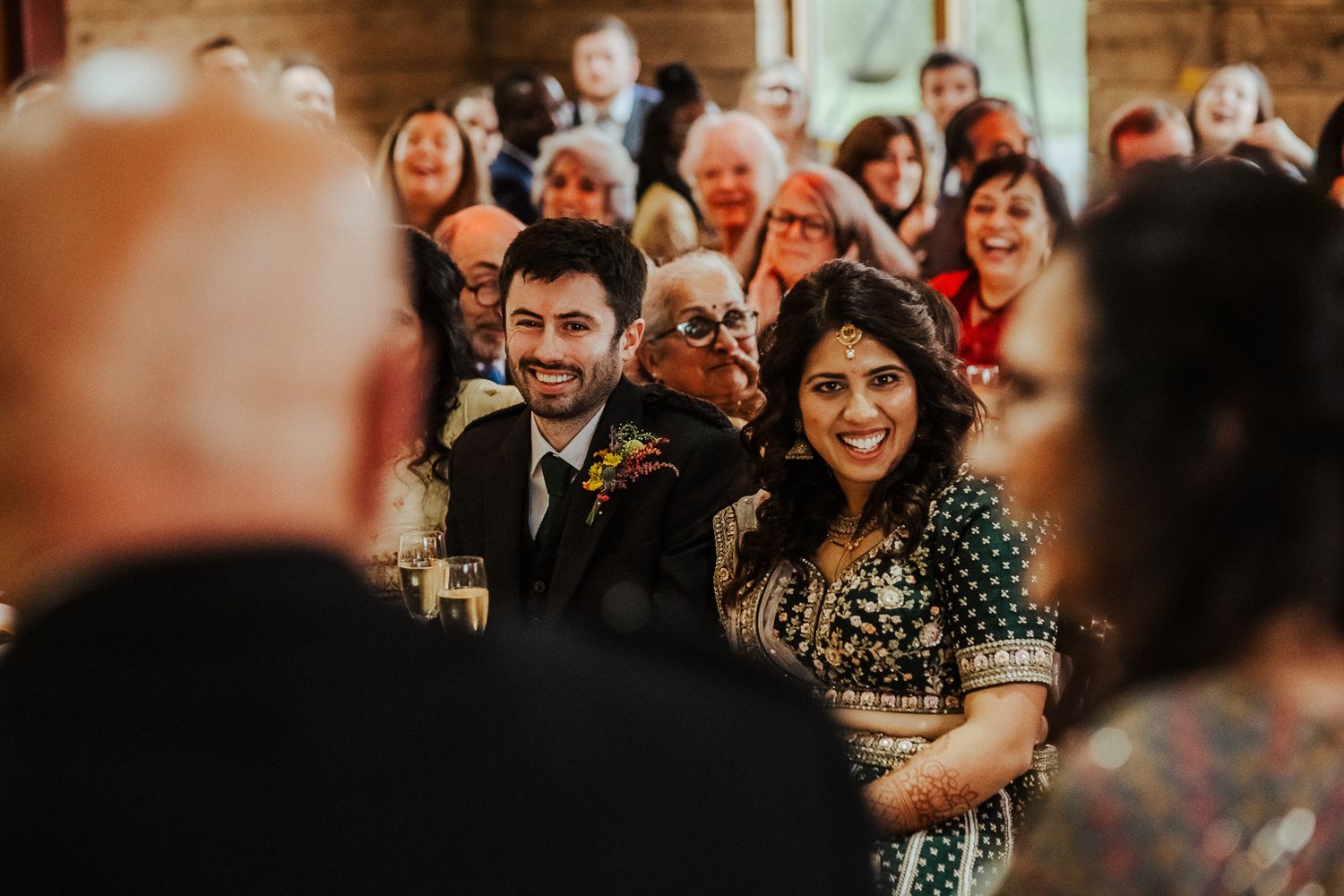 Wedding reception guests laughing and celebrating in a rustic wooden venue.