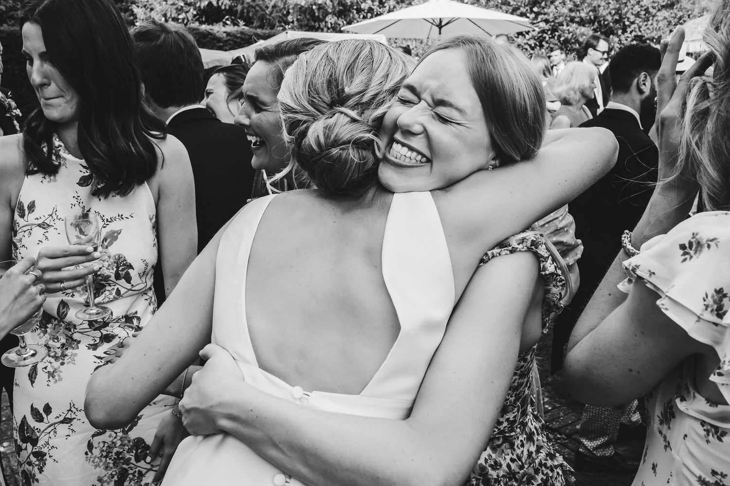 A candid black and white moment of two guests embracing at an outdoor celebration.