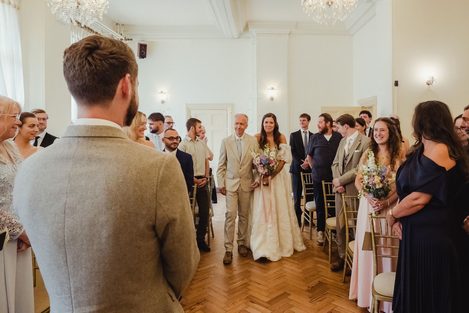 Wedding guests dance and celebrate together in an elegant ballroom with hardwood floors and chandelier lighting.