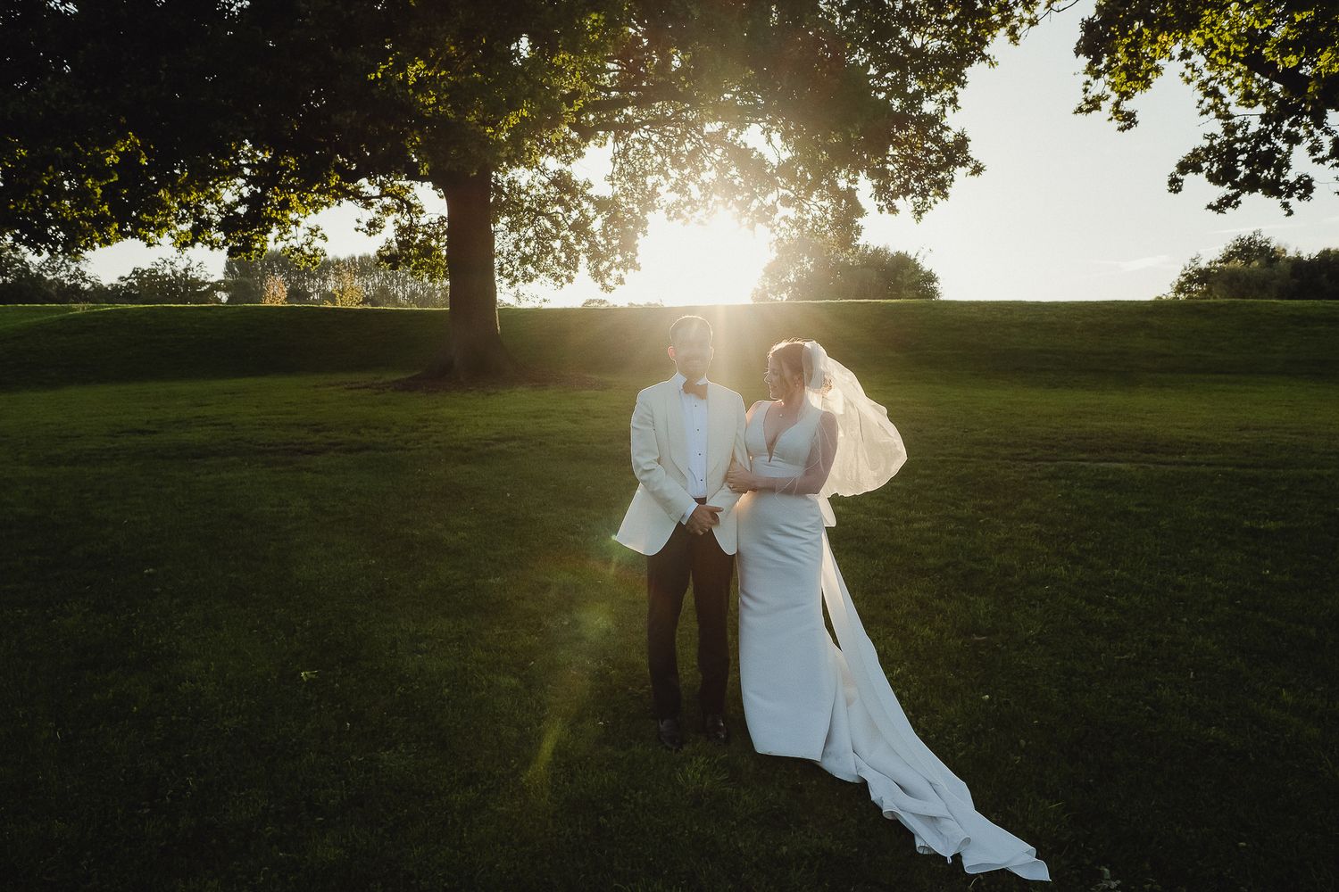 A romantic sunset photoshoot in a grassy field with soft golden light filtering through the trees.