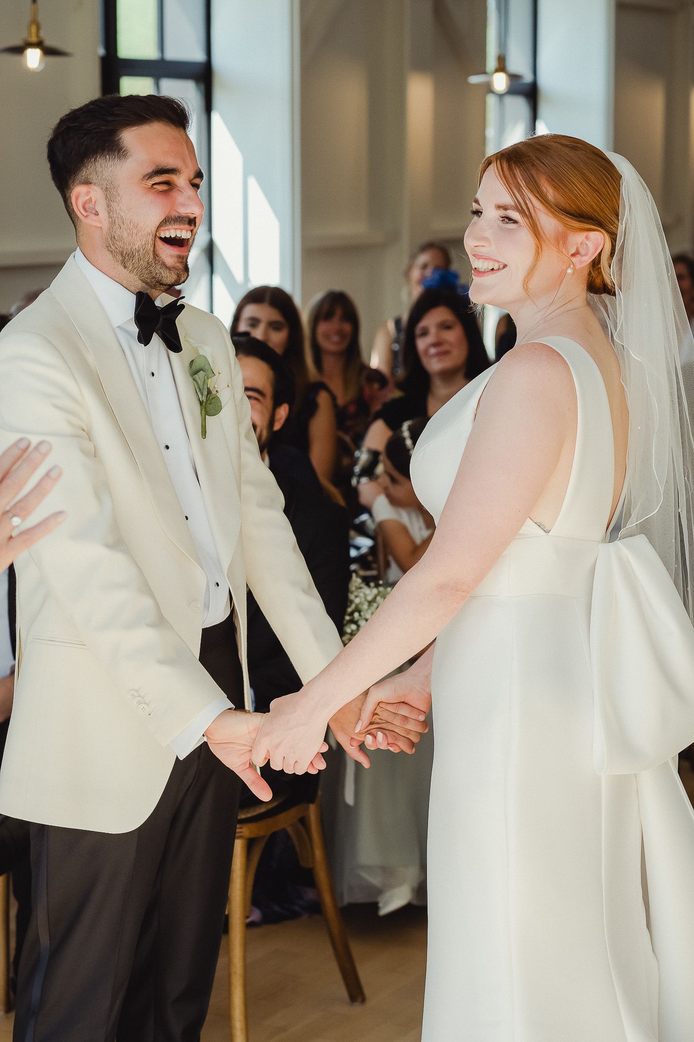 Joyful newlyweds share a candid moment during their wedding reception, laughing together in white formal attire.