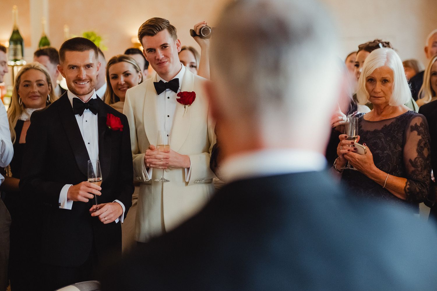 Wedding guests raise their glasses in celebration during a toast at an elegant indoor reception.
