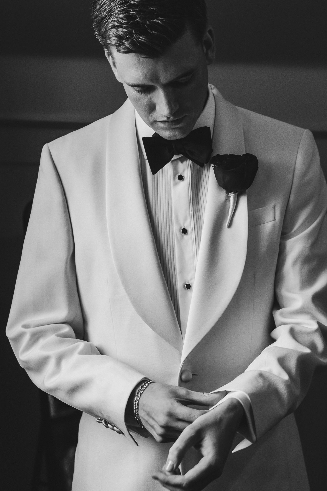 Black and white photo series showing details of someone adjusting their formal white tuxedo jacket and bow tie.