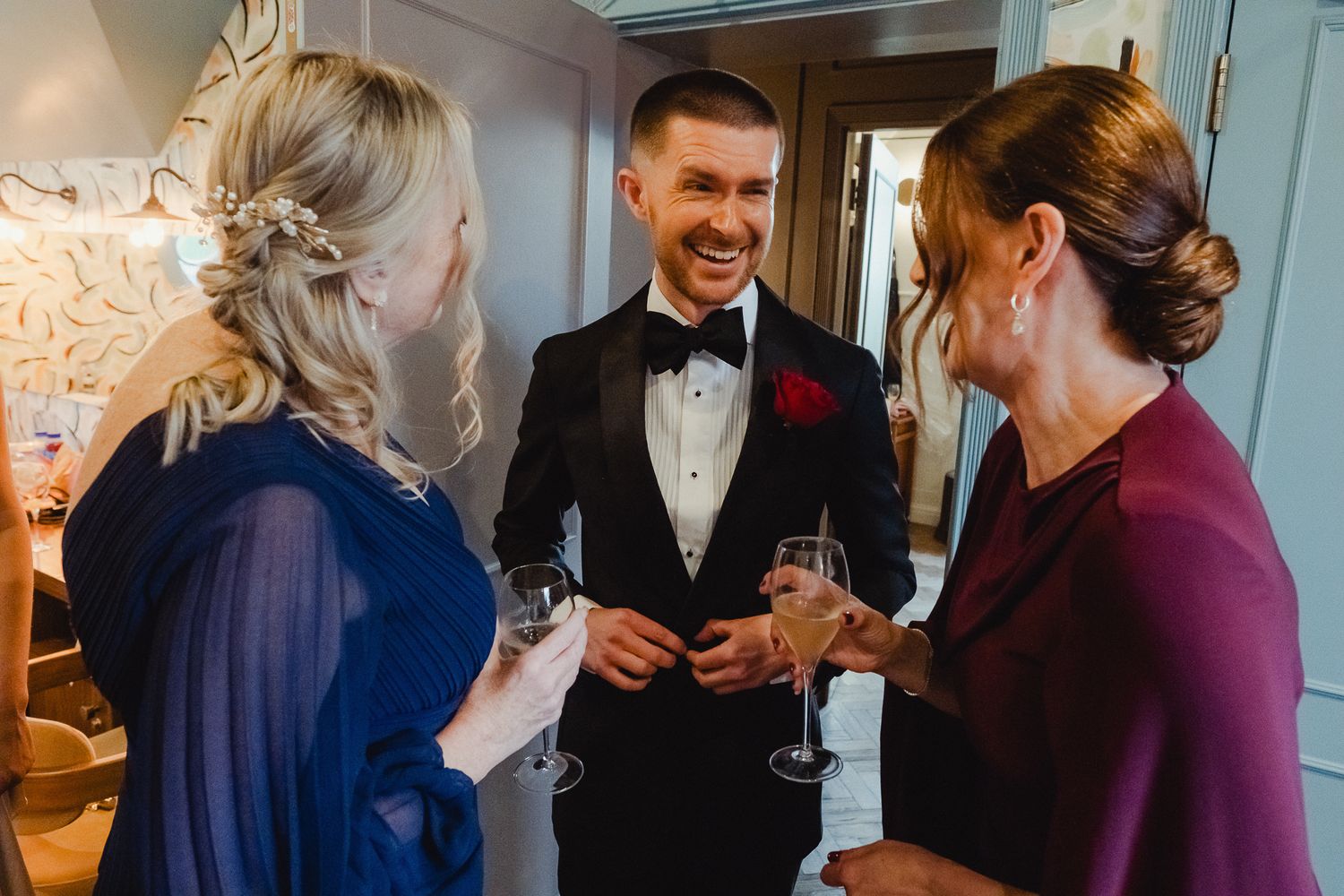 A group of people in formal attire gather at an event, holding drinks and engaged in conversation.
