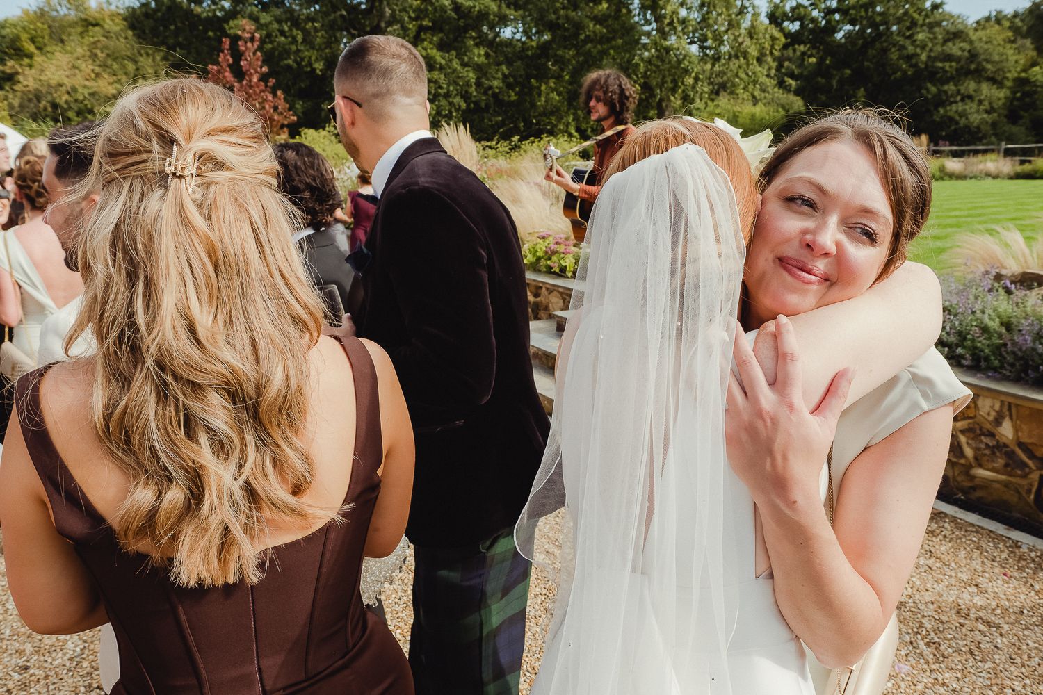 Wedding guests gather outdoors in a garden setting during a celebratory reception event.