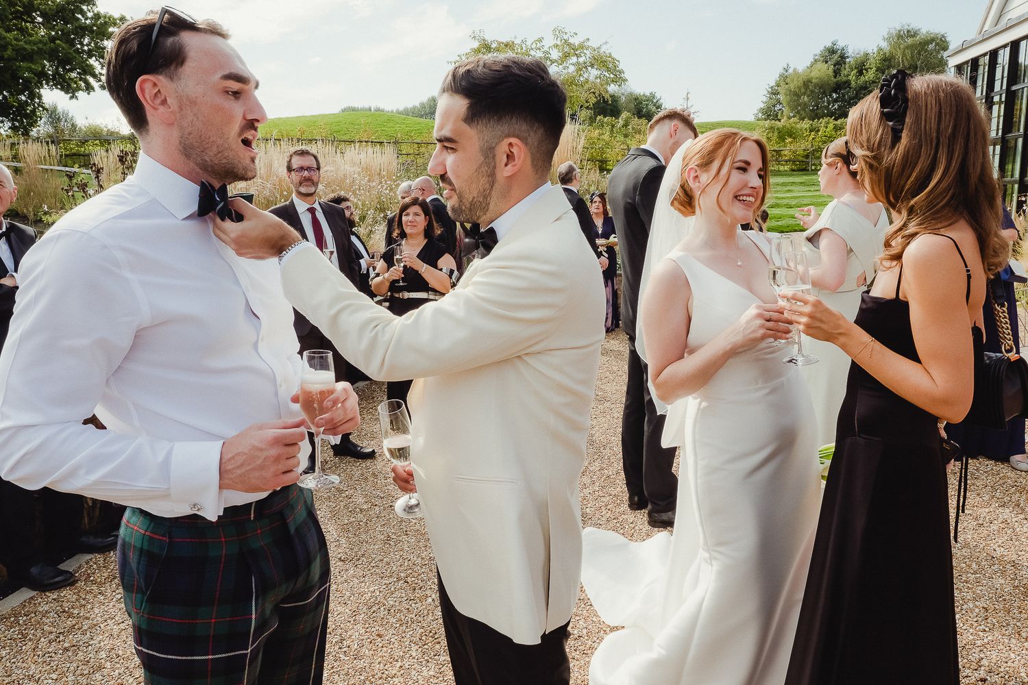 Wedding guests celebrate and mingle during an outdoor cocktail reception on a sunny day.
