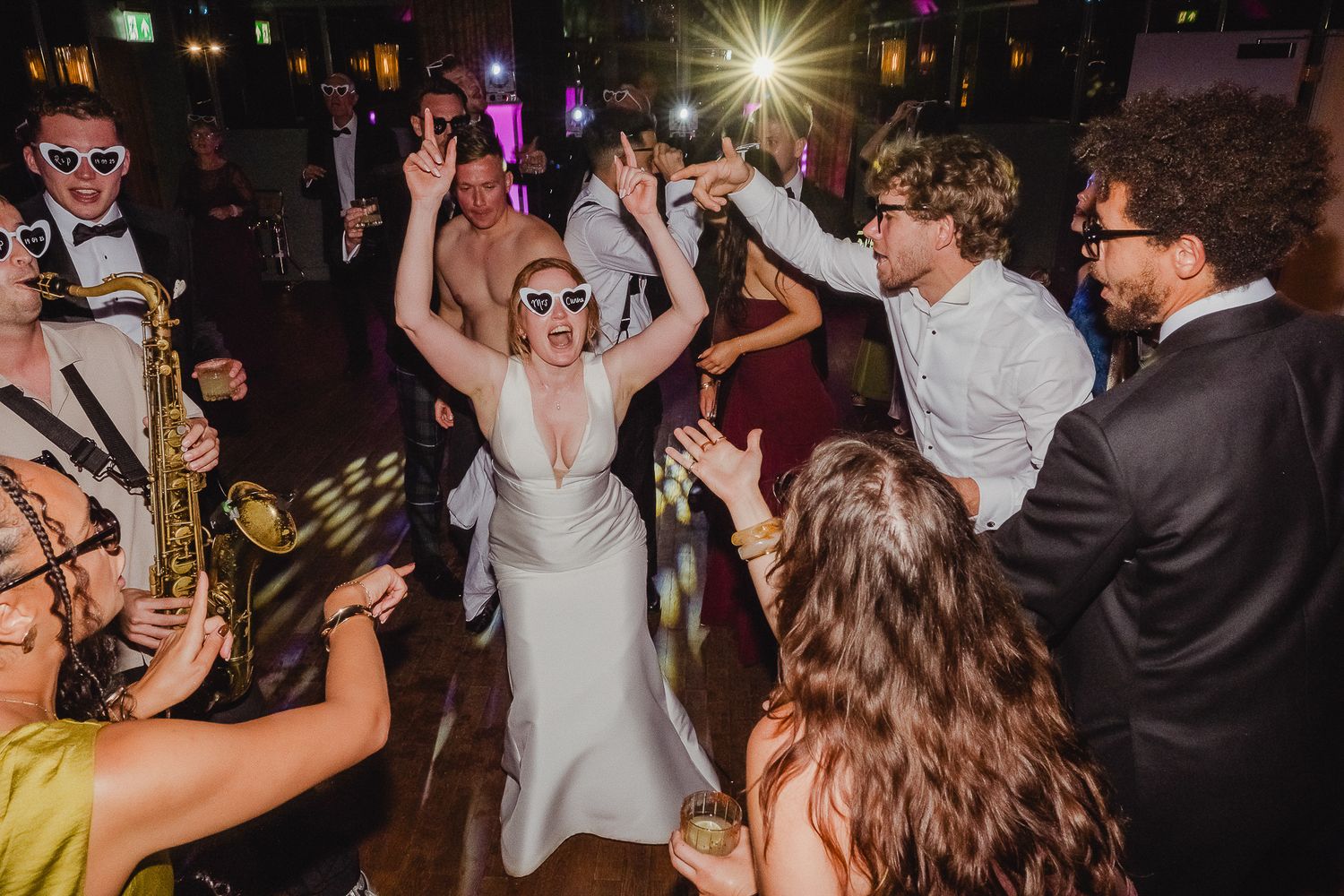 Energetic wedding guests dancing and celebrating on a dimly lit dance floor during a lively reception party.
