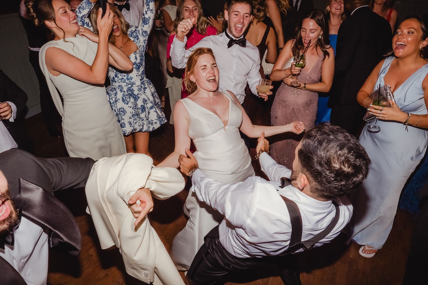 Energetic wedding reception party with guests dancing and having fun on a dimly lit dance floor.