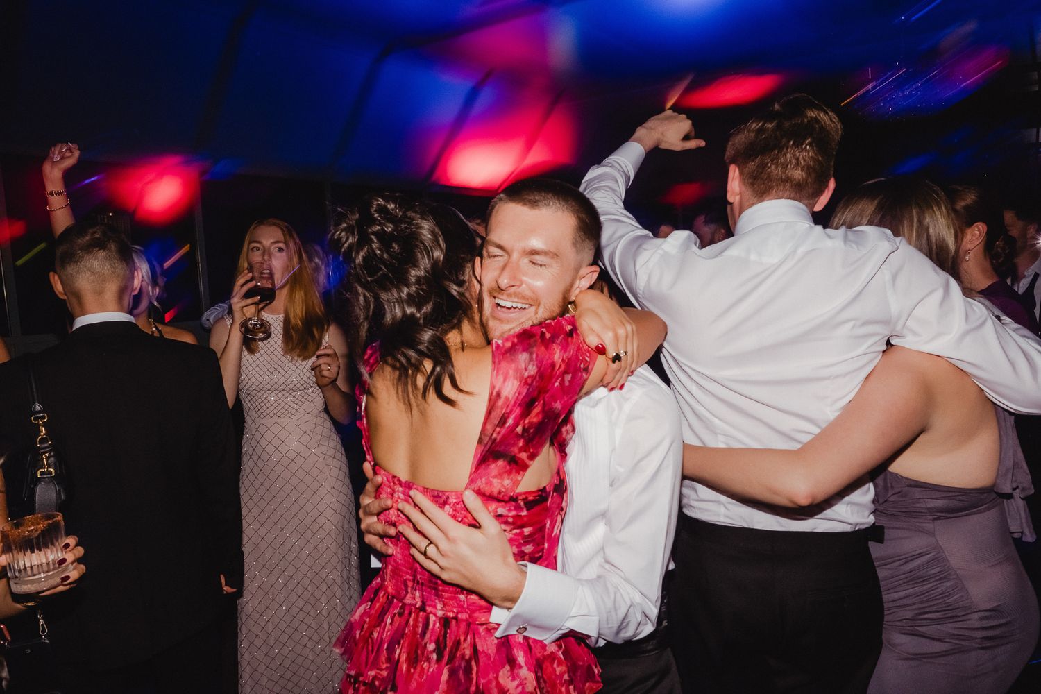 Couples dancing together at a nighttime event with colorful pink and blue lighting in a dark venue.