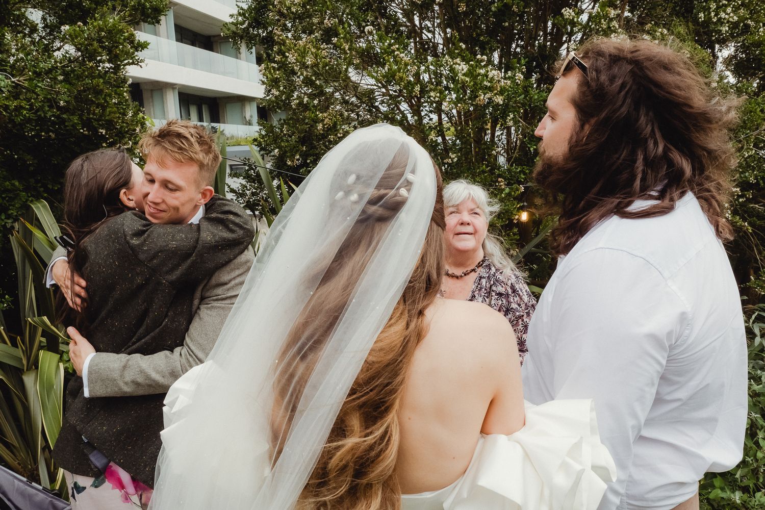 A joyful wedding celebration outdoors with guests sharing hugs and laughter on a sunny day.