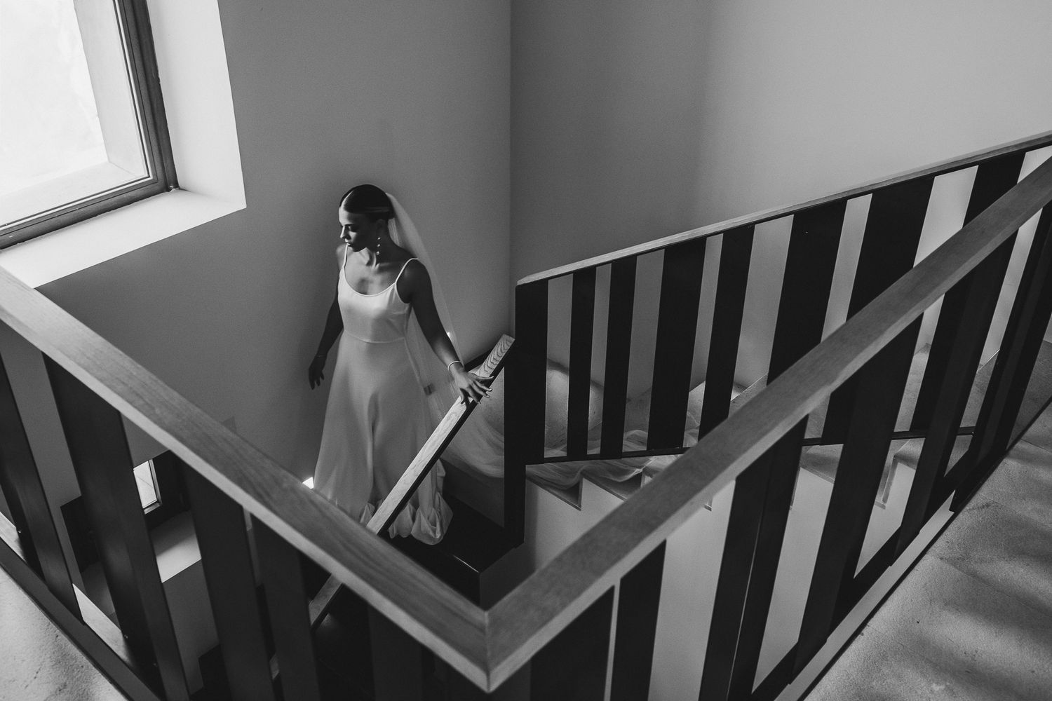 Black and white photograph showing a staircase with wooden railings and steps leading up in a spiral pattern.