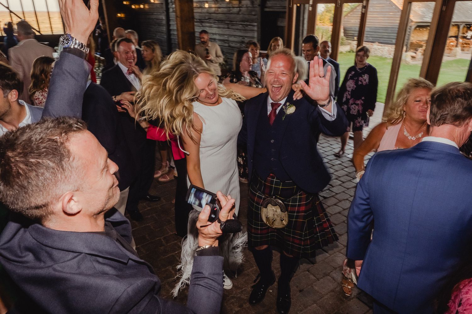 People dancing and celebrating at a wedding reception in an indoor venue with dark lighting.