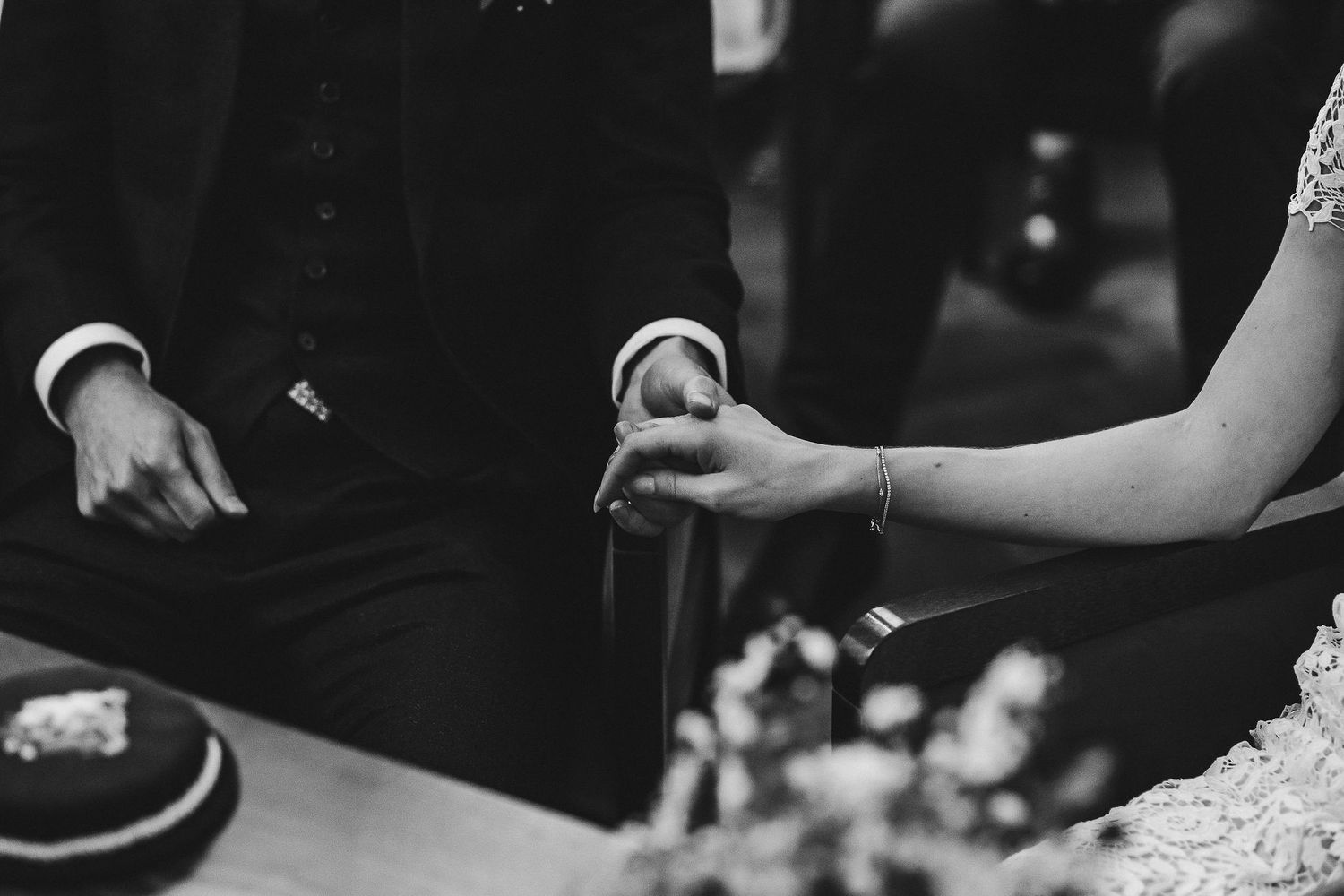 Black and white photo of hands cutting a wedding cake together at a reception celebration.