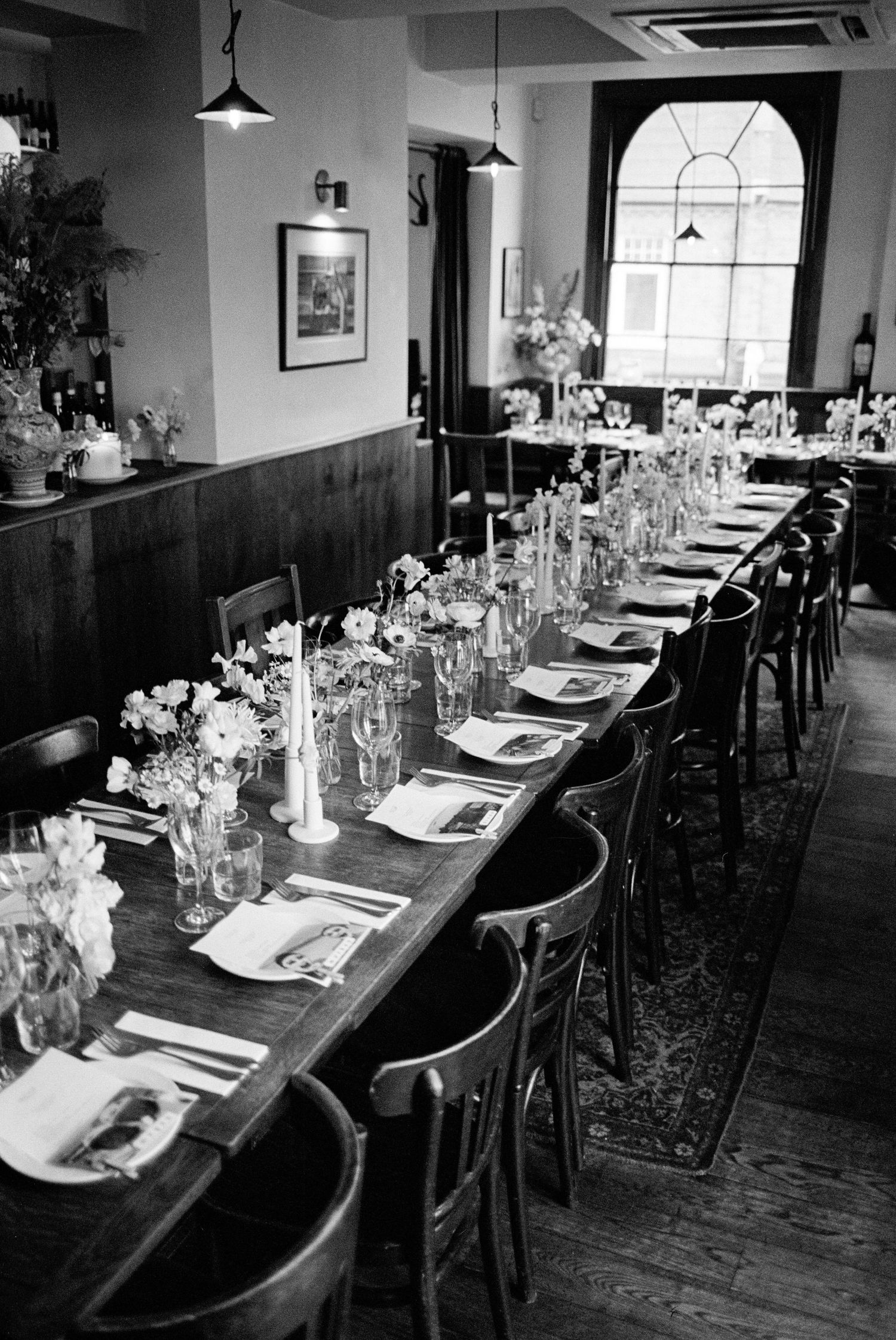 Black and white photo of an elegant long dining table set for a private event in a cozy restaurant interior.