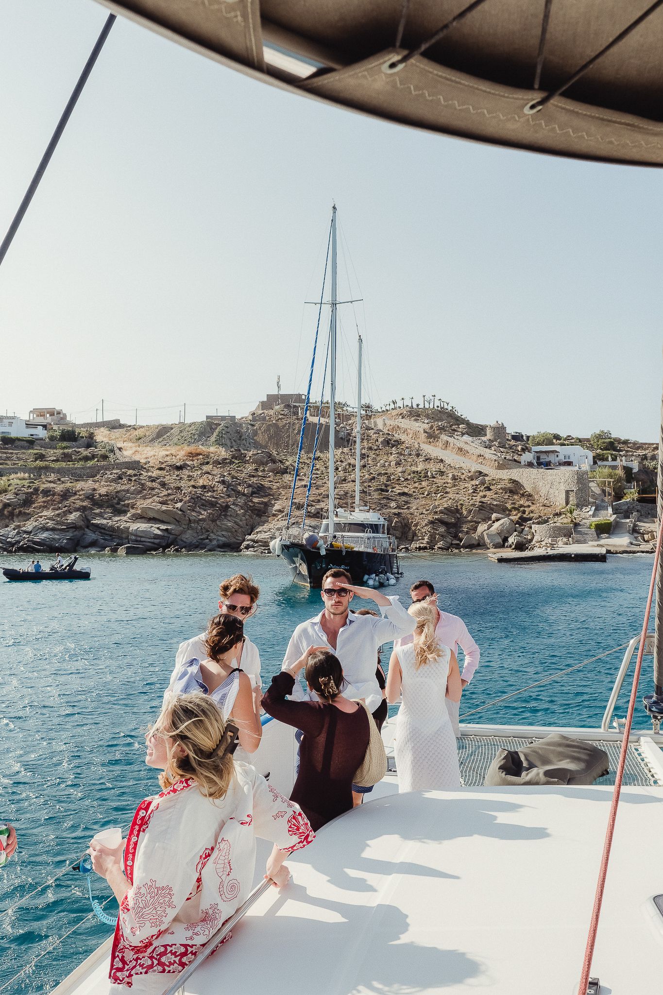 Wedding guests enjoying a boat tour along rocky Mediterranean coastline with yachts and blue waters in view.