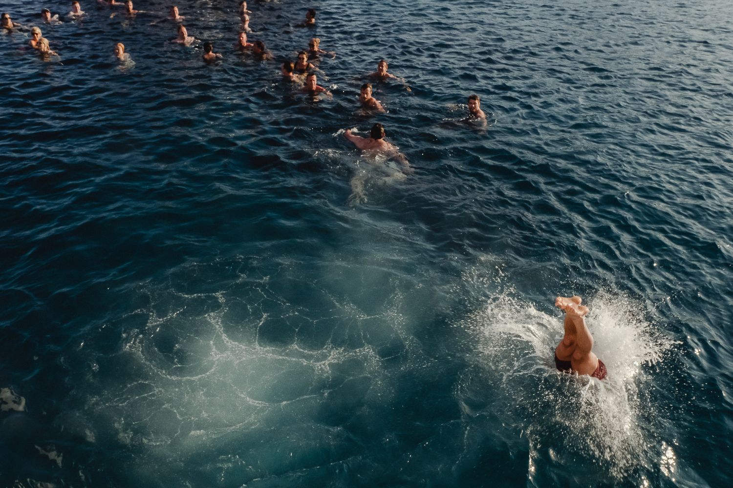 Swimmers create splashing patterns in dark blue ocean water during an open water swimming event.