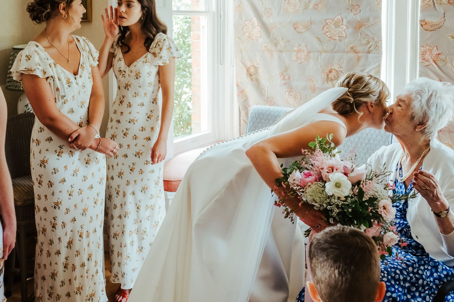 A bride in a white dress bends over laughing with bridesmaids in floral dresses.