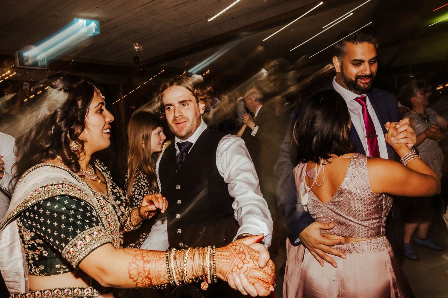 Guests dancing energetically at a multicultural wedding reception with traditional Indian attire.