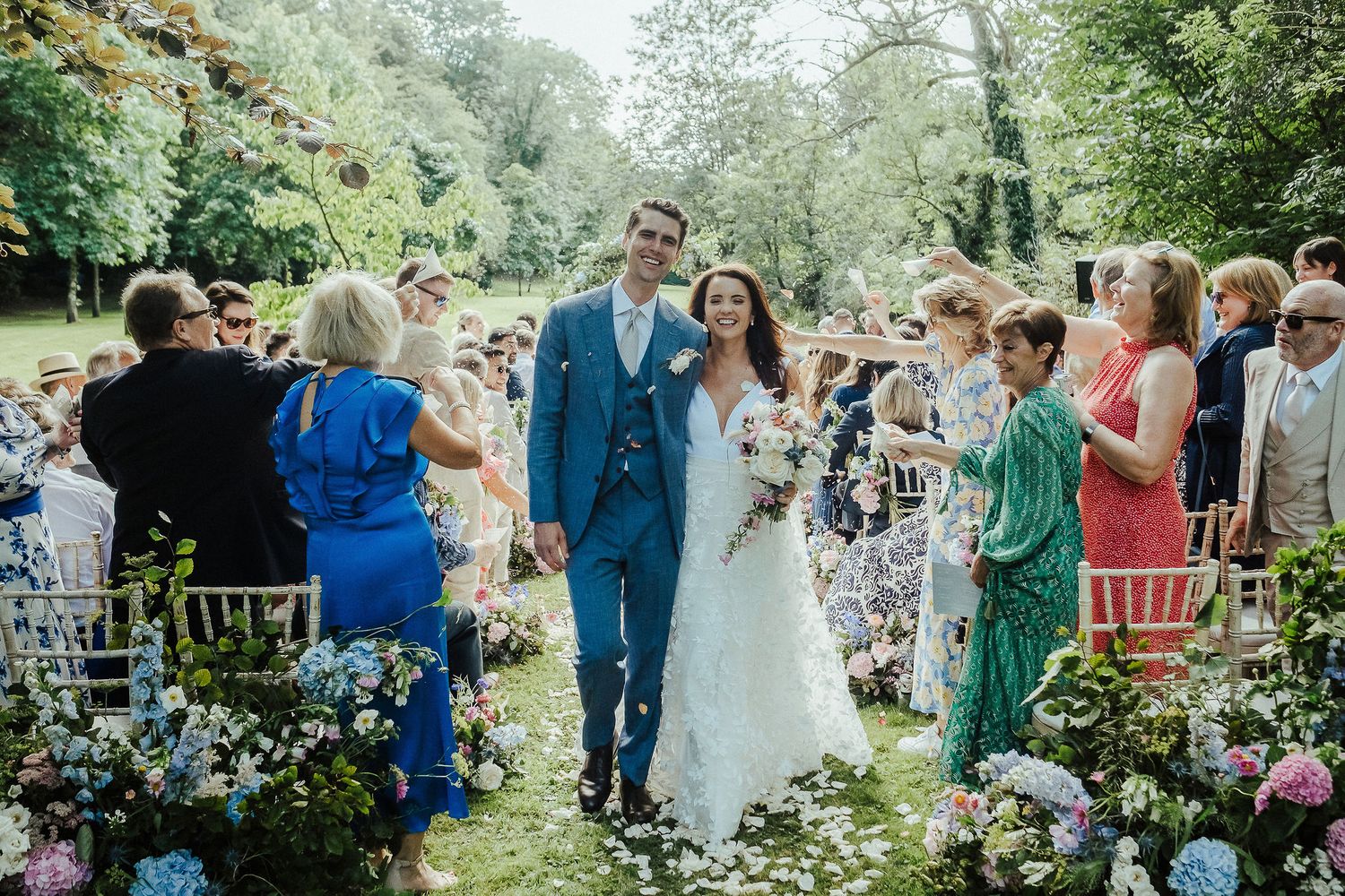 Wedding ceremony recessional through garden path lined with guests and flowers.
