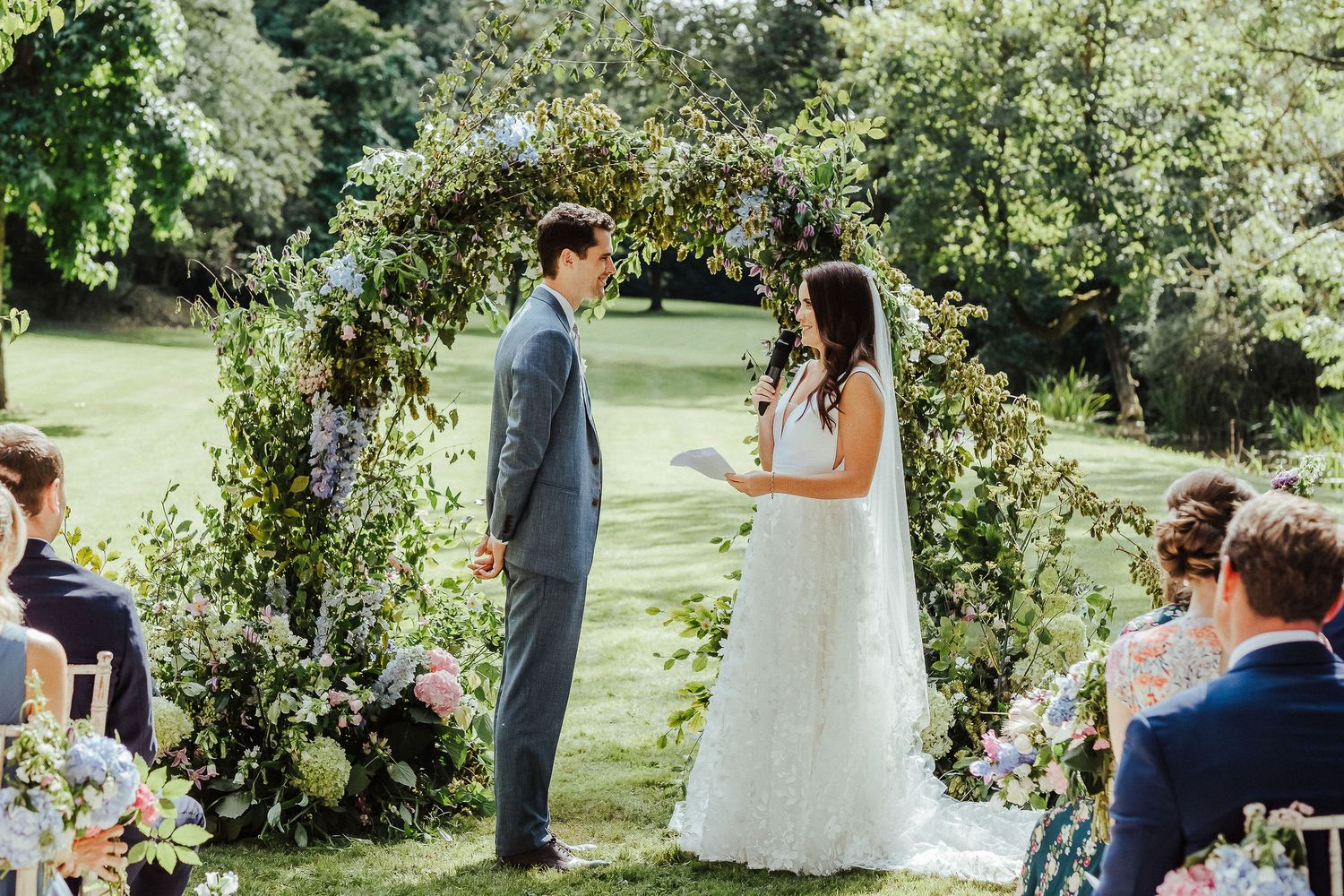 A couple exchanges vows under a floral arch during an outdoor garden wedding ceremony.