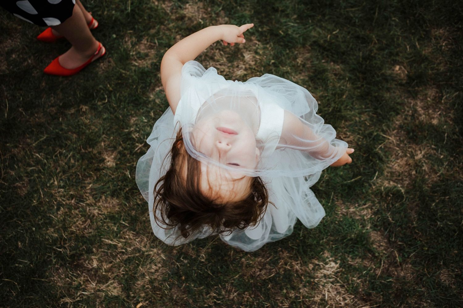 Overhead view of bride in white dress lying on grass in artistic pose.
