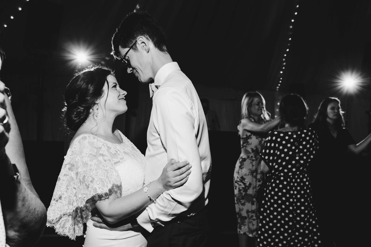 Couples dancing at a dimly lit wedding reception with string lights overhead.