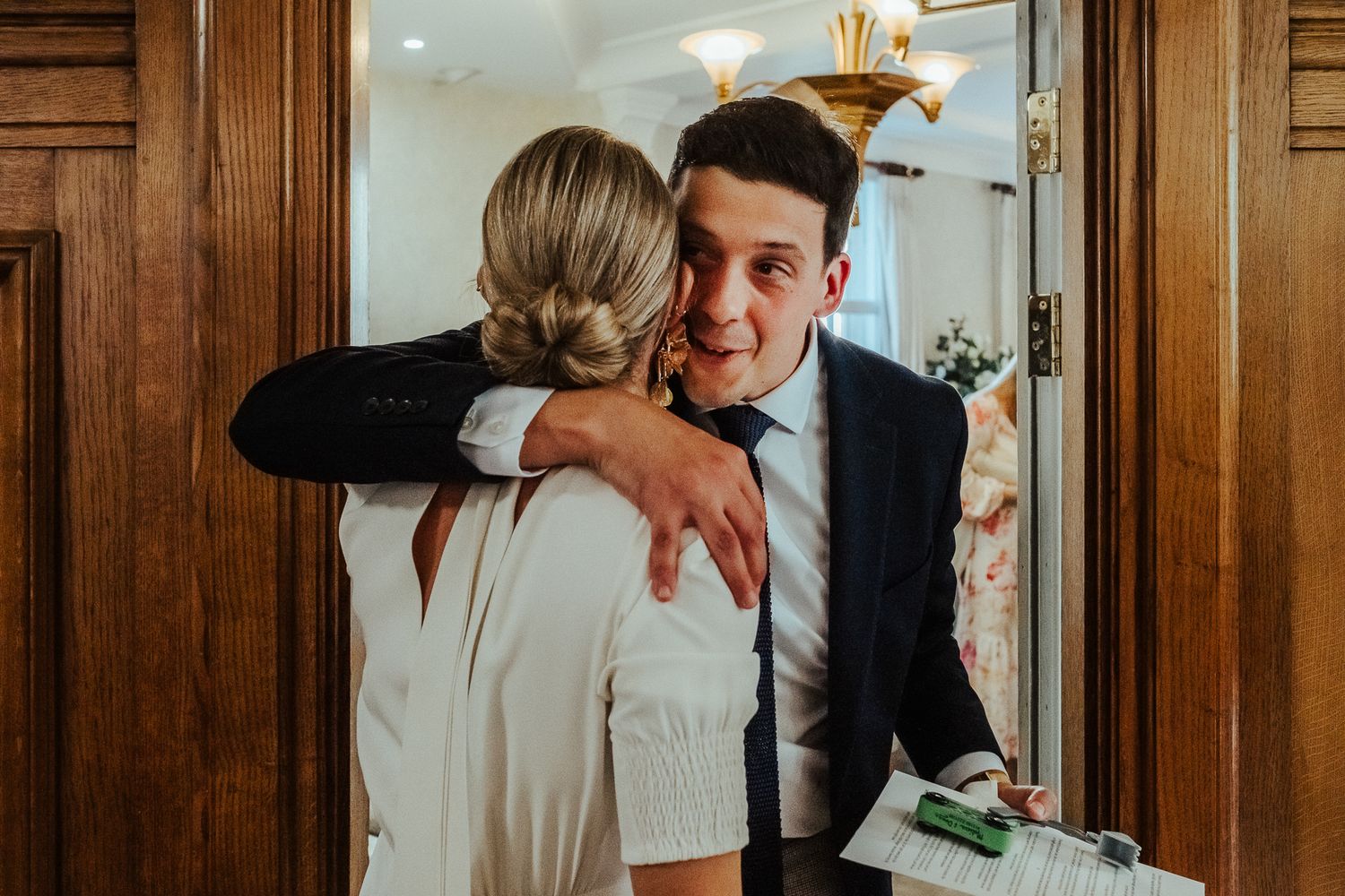 Two people embrace and laugh together in a wood-paneled room with warm lighting.