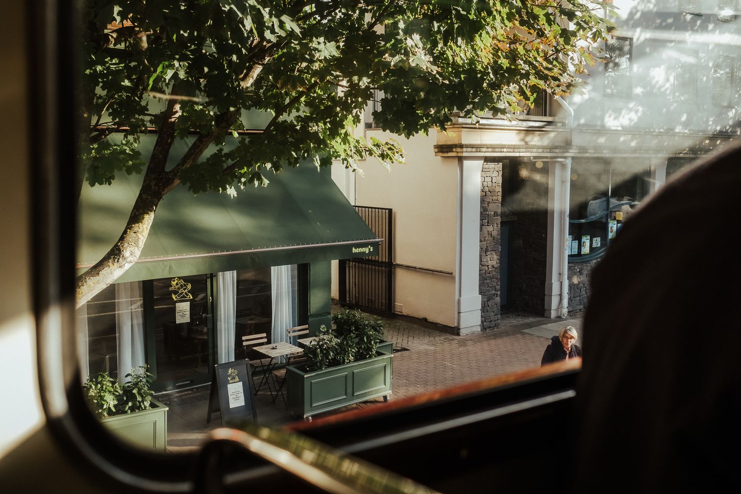 View through window of a charming cafe storefront with green awning and window planter boxes on a brick walkway.