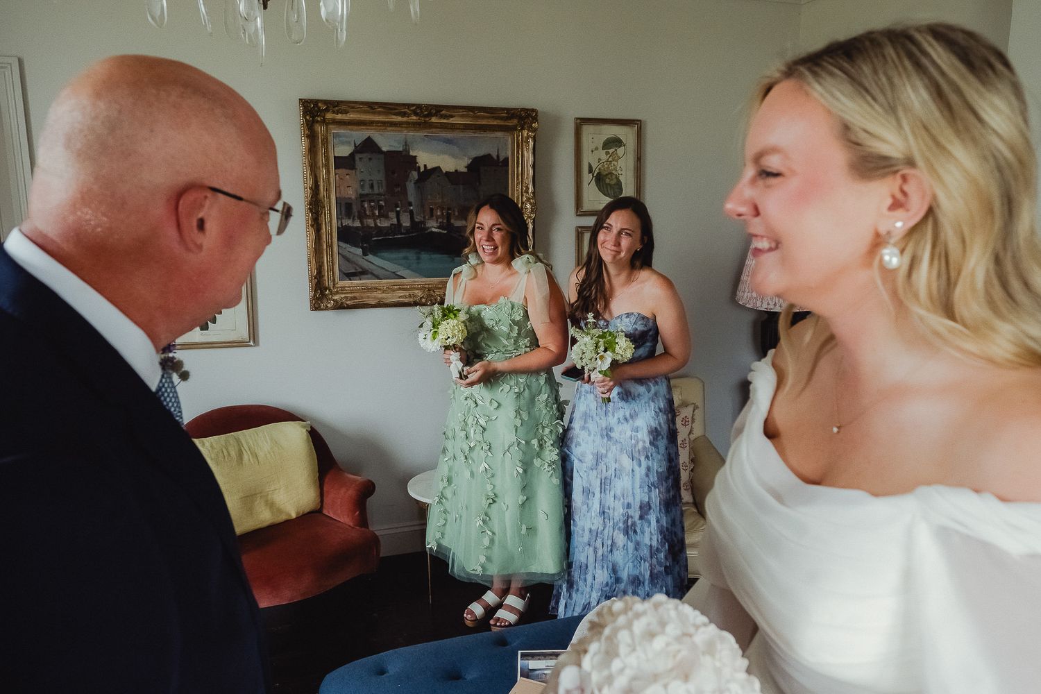 A candid moment at a wedding with bridesmaids in pastel dresses and a bride in white sharing a joyful interaction.