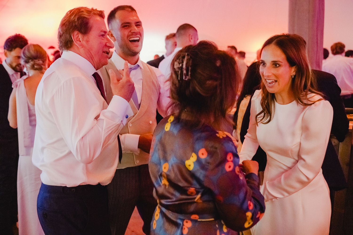 People dancing and celebrating at a lively wedding reception with colorful lighting and a festive atmosphere.