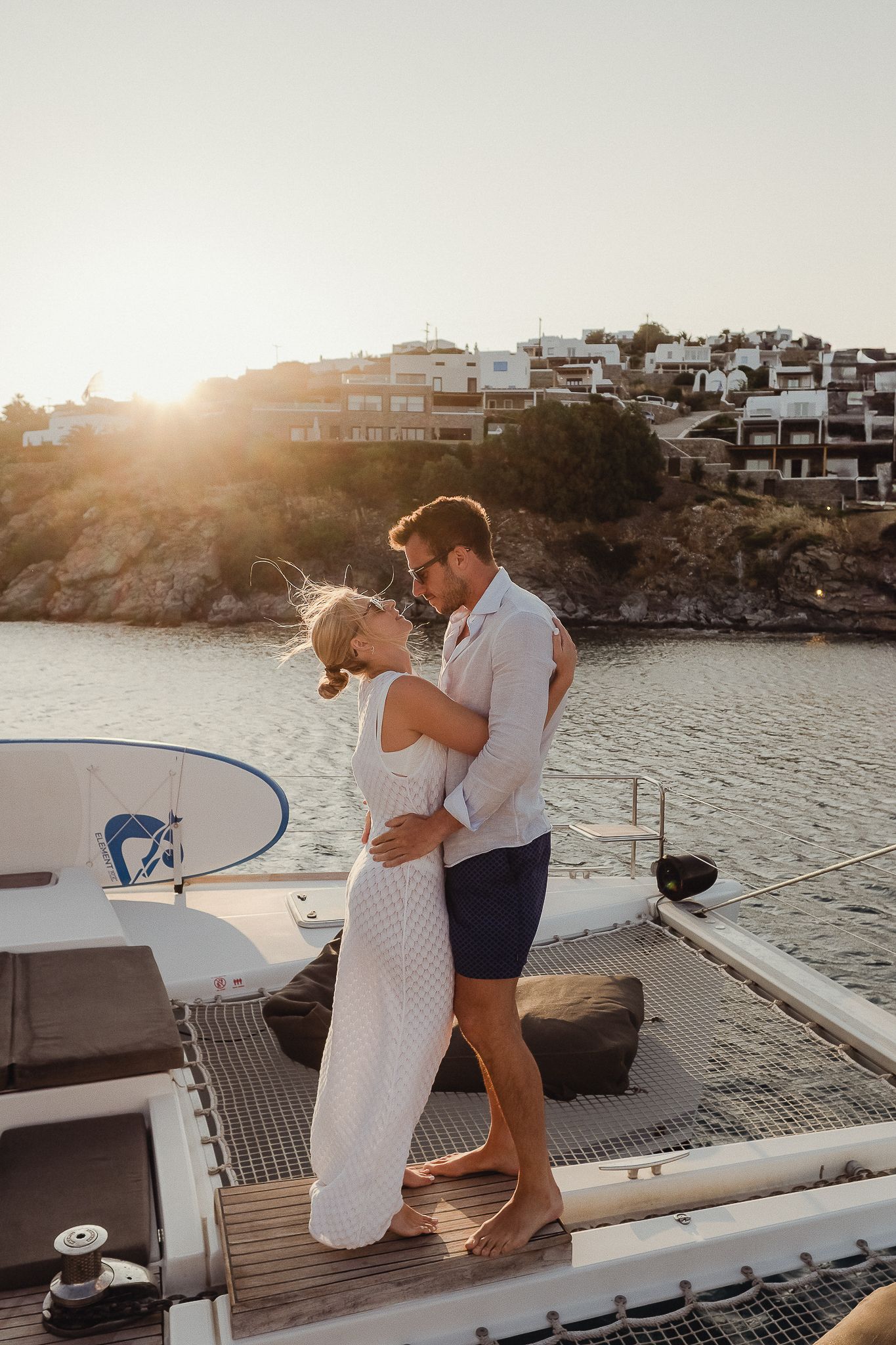 Romantic sunset yacht photoshoot featuring couple embracing on boat deck with coastal homes in background.