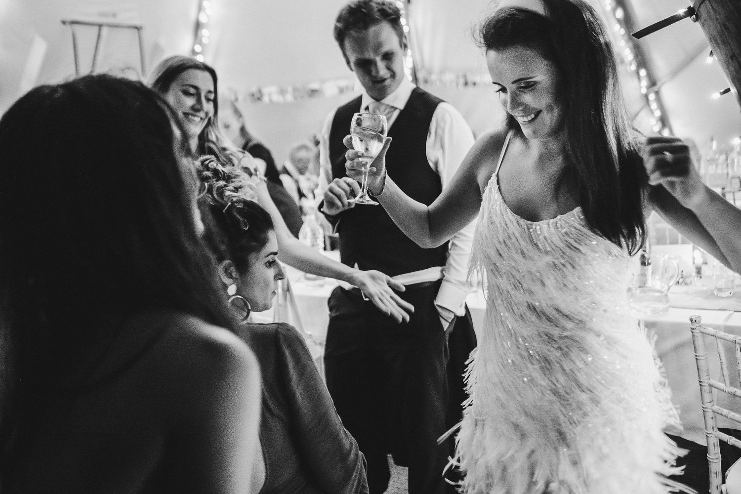 Wedding reception guests share joyful moments while dancing in black and white photography.