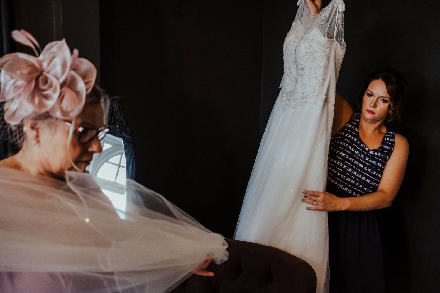 Wedding dress being prepared and adjusted in dramatic lighting.