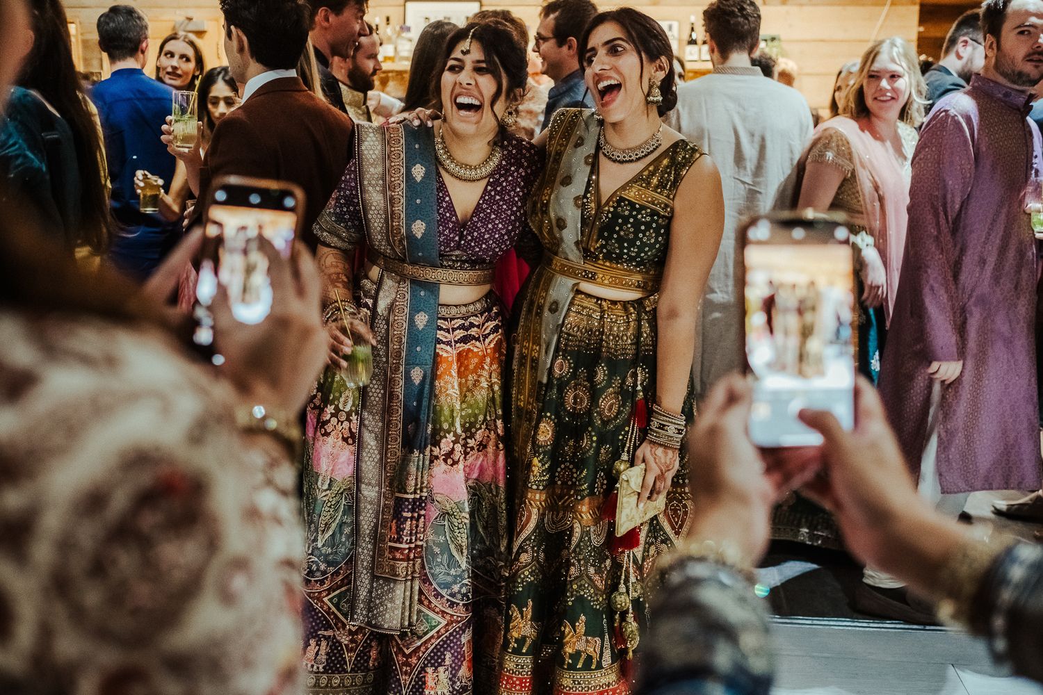 People in colorful traditional outfits gather and socialize at a festive indoor celebration.