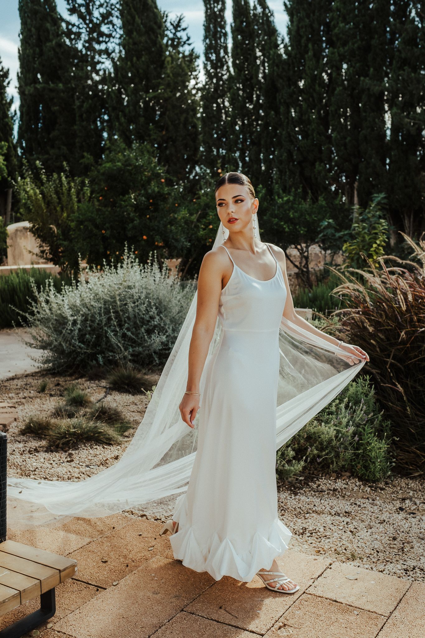 A flowing white wedding dress with a long train captured in a garden setting with natural greenery and wooden walkways.