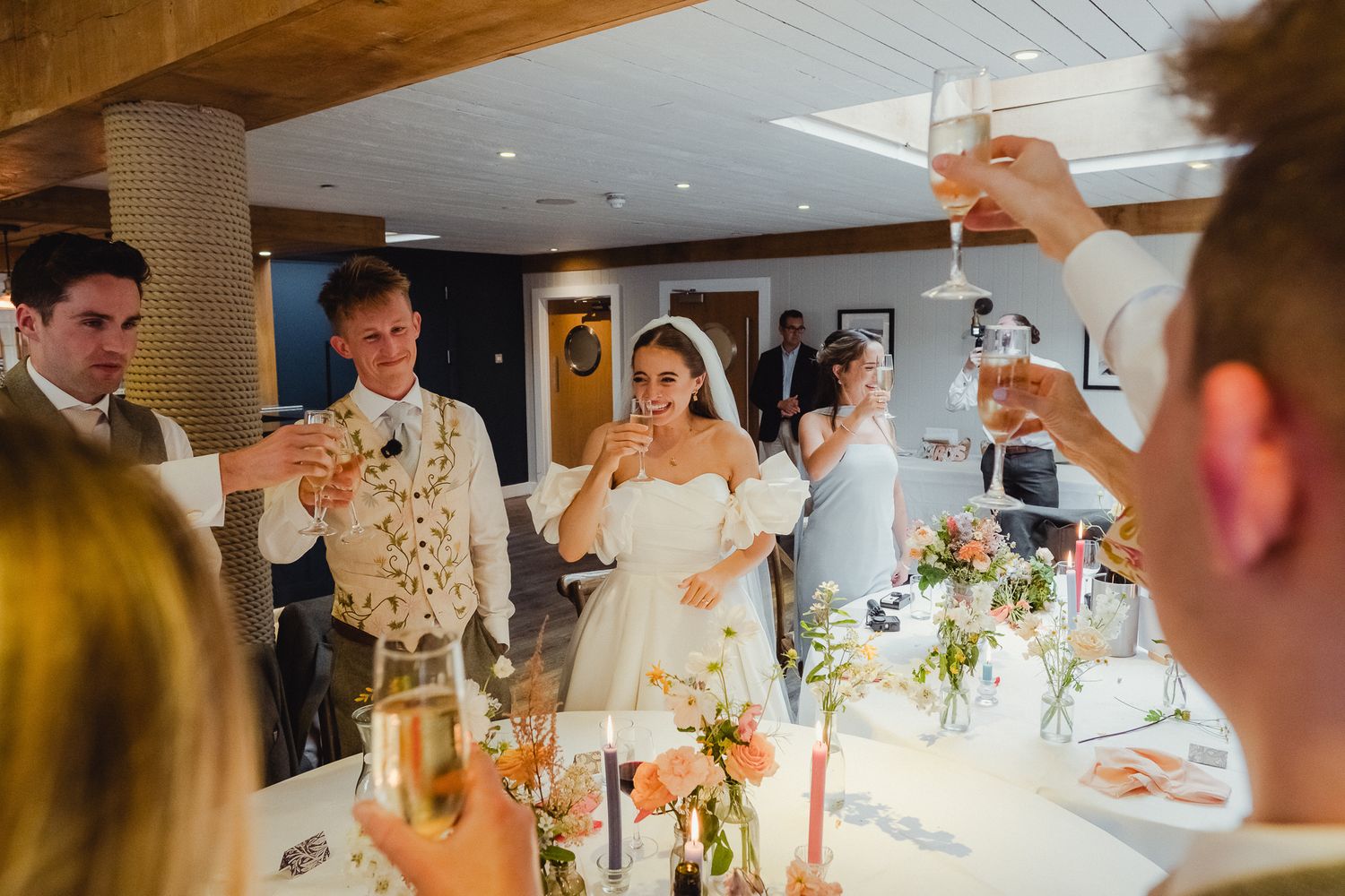 Wedding guests gather around a long table during a reception dinner with candles and elegant place settings.