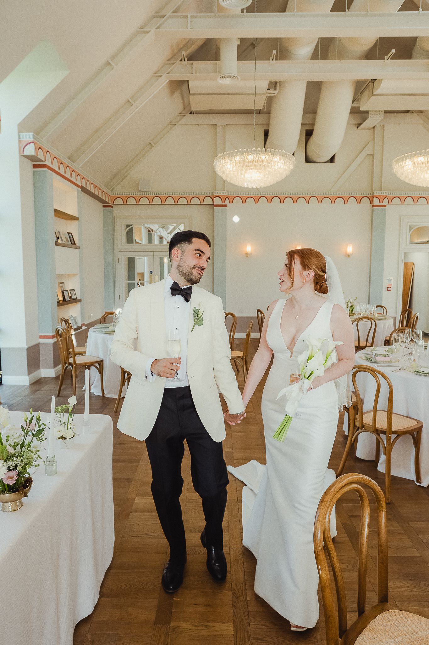 A couple shares a romantic dance moment in a bright white reception venue with wooden floors and elegant decor.