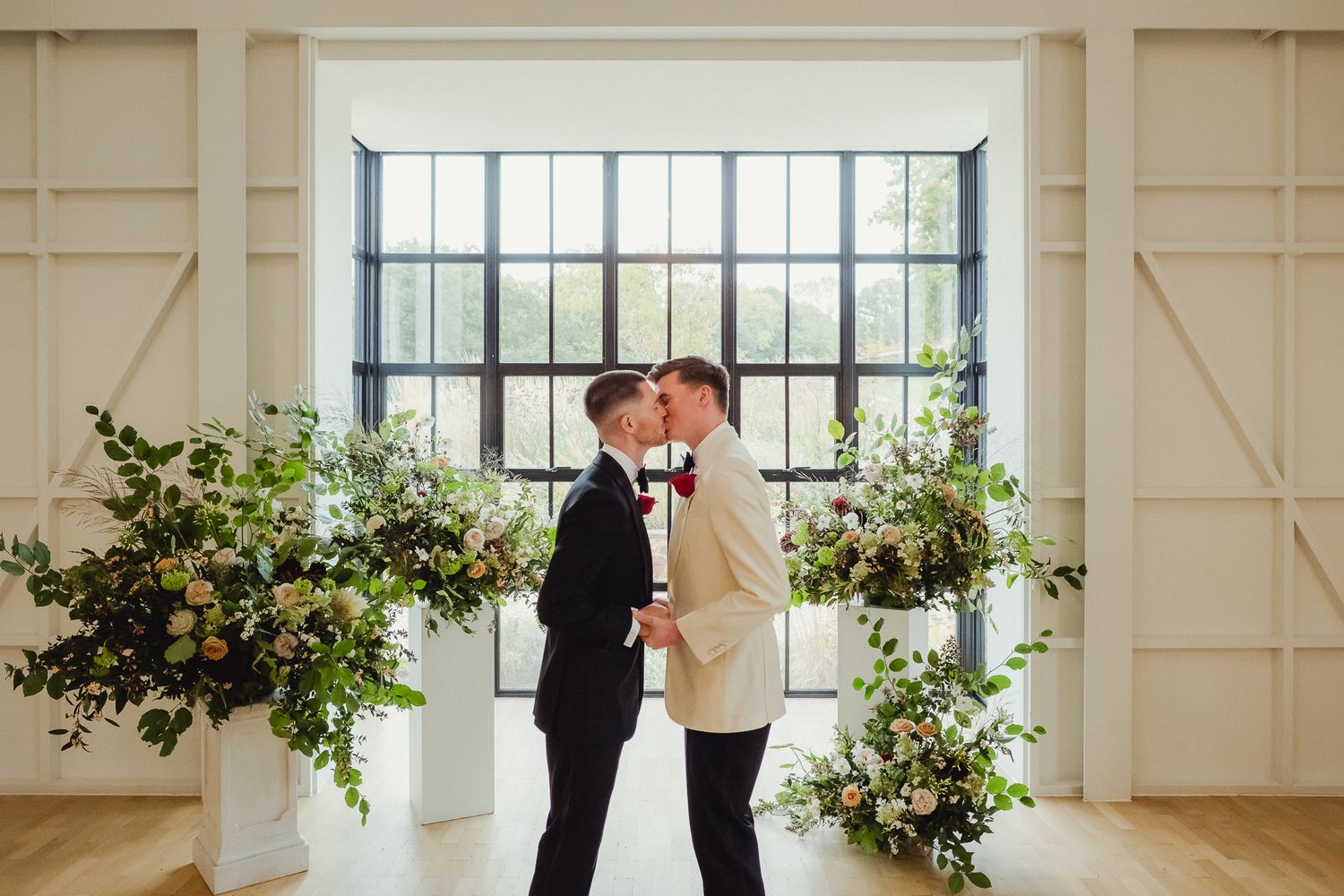 Couple shares romantic moment in bright white room with industrial windows and elegant floral arrangements.