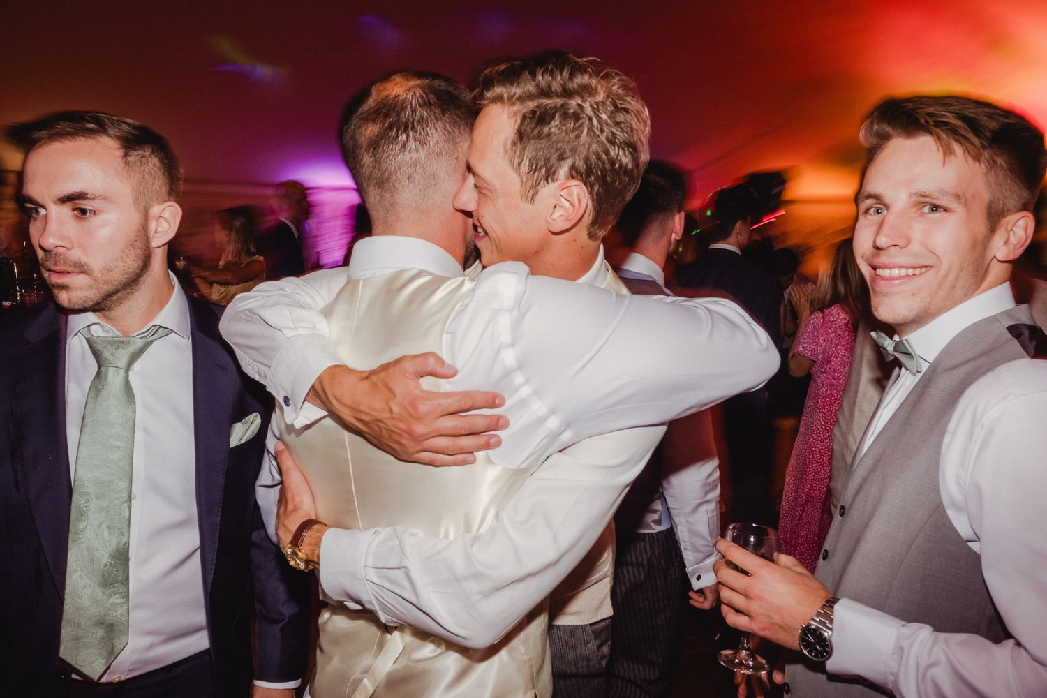 A series of candid moments at a wedding reception showing people embracing and dancing under colorful lighting.