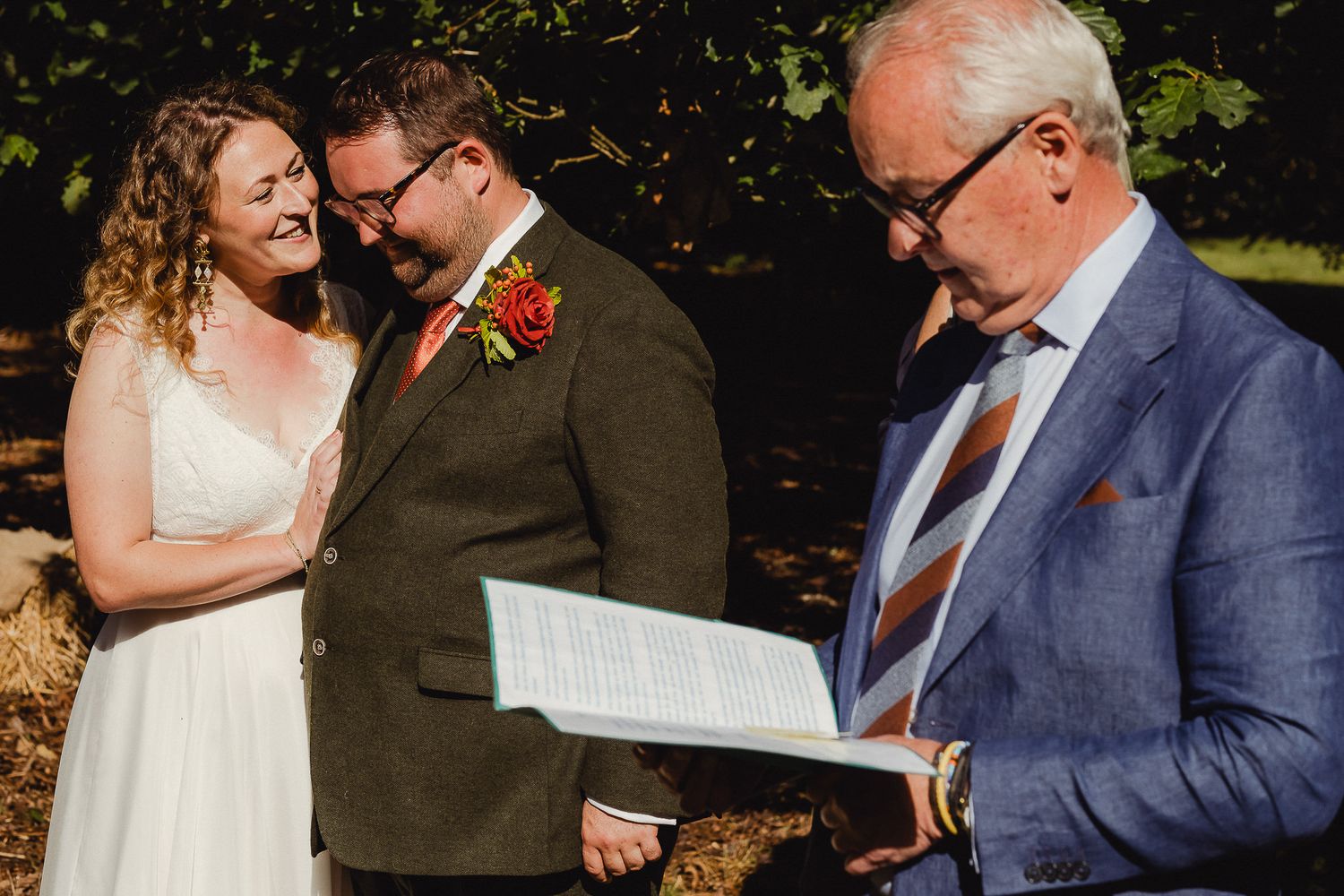 Couple shares a tender moment while reading documents together during an outdoor ceremony.