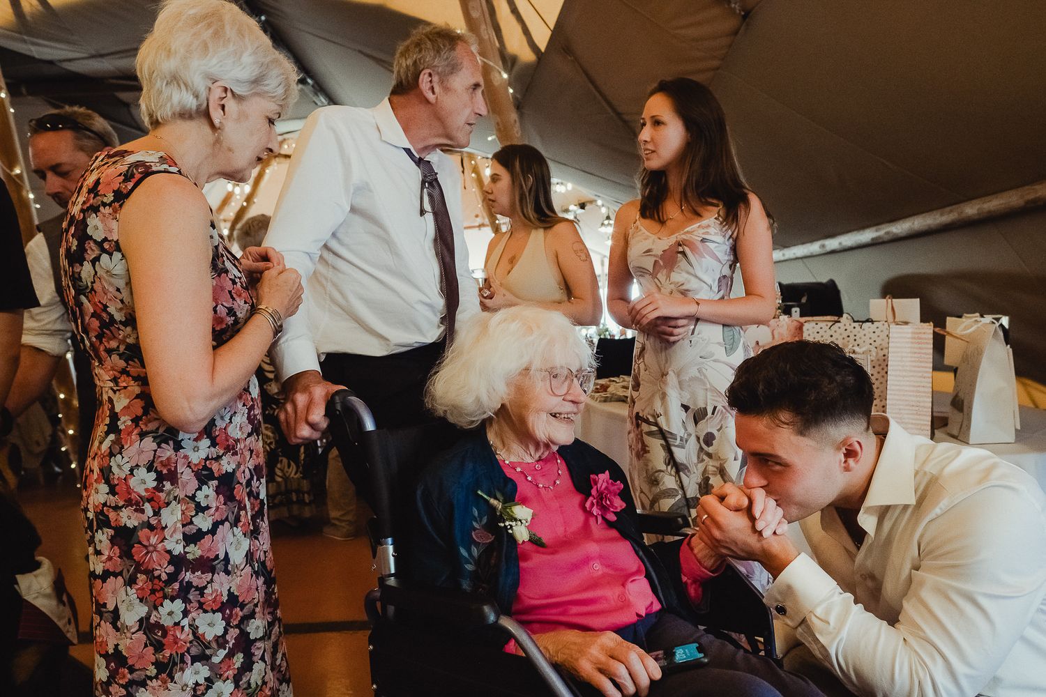 Wedding guests gather in a reception venue, sharing drinks and conversations in a warm, dimly lit atmosphere.
