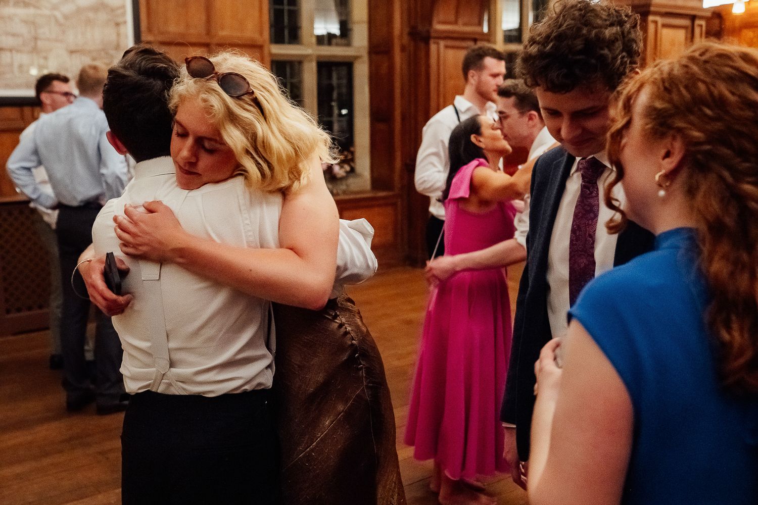 Guests hugging and socializing at an elegant wedding reception in a wood-paneled venue.
