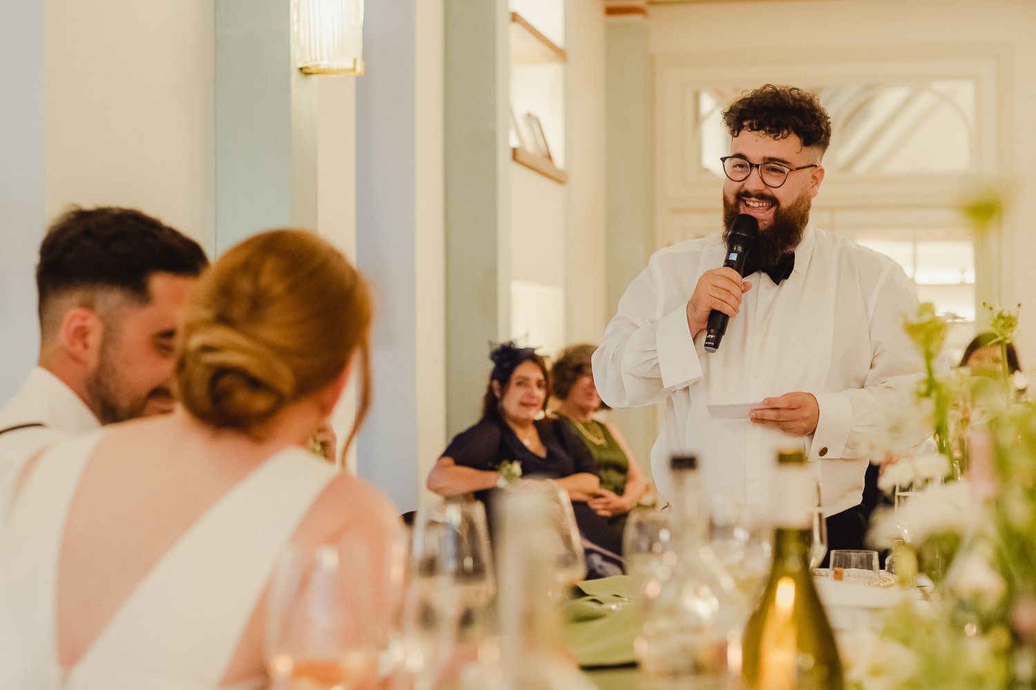 Wedding guests enjoying a candlelit dinner reception at elegant tables decorated with white floral centerpieces.
