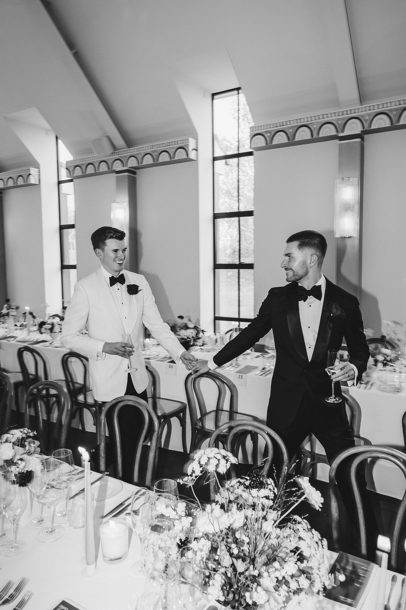 Two people in formal attire stand at an elegant reception table with floral centerpieces and place settings.